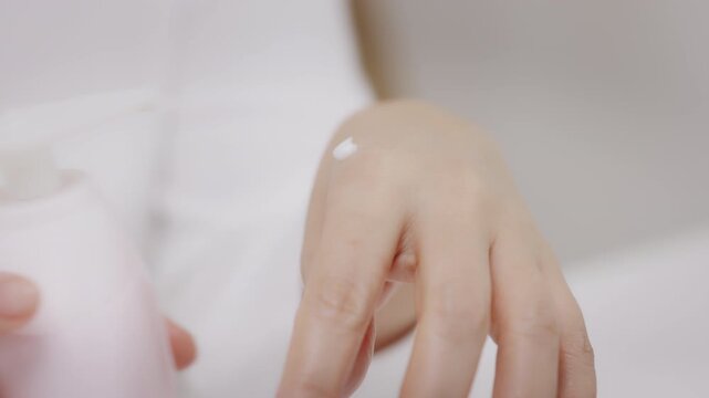 Close-up shot of a mature woman gently applying skincare cream to the back of her hand during routine care.