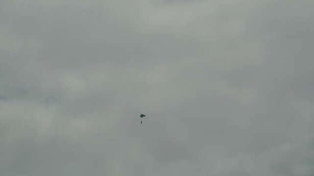 Distant view of a Guardia Civil parachutist descending with a canopy wing through an overcast grey sky during the Gijon Air Show (Festival Aereo de Gijon) in Asturias, Northern Spain.
