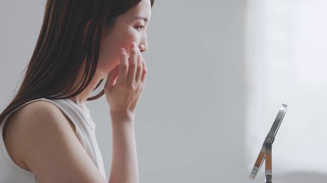 鏡を見ながら頬に触れて肌を確認する女性の横顔