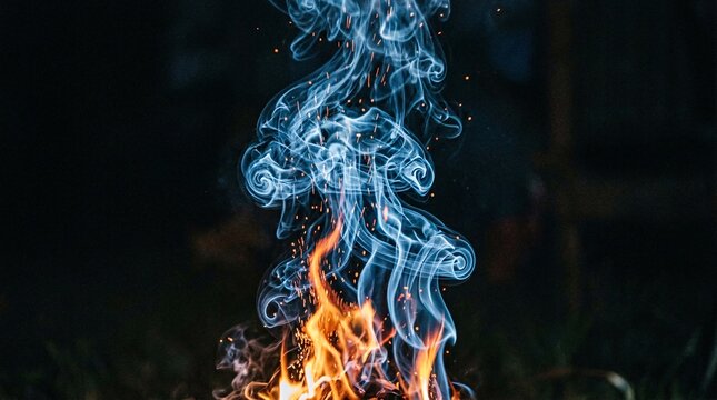 Blue smoke swirling gracefully upward from a small outdoor campfire flame in the dark night.