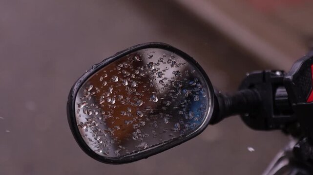 Close up of a motorcycle side mirror covered in raindrops with slow motion rain