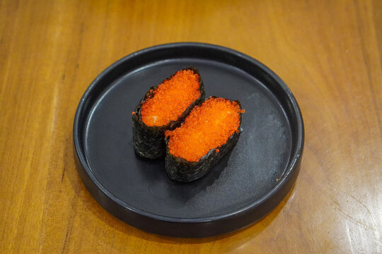 Tobiko gunkan sushi with bright orange flying fish roe wrapped in nori, served on a black plate with chopsticks and mayonnaise at a Japanese restaurant.