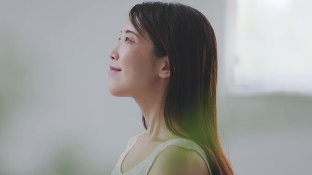 観葉植物越しに頬へ触れる女性の美容イメージ