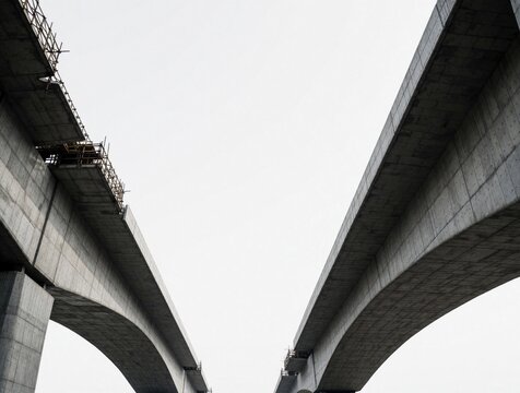 Unfinished concrete bridge sections rise against overcast sky. Infrastructure project shows stark geometry of construction. Heavy concrete structures await completion.