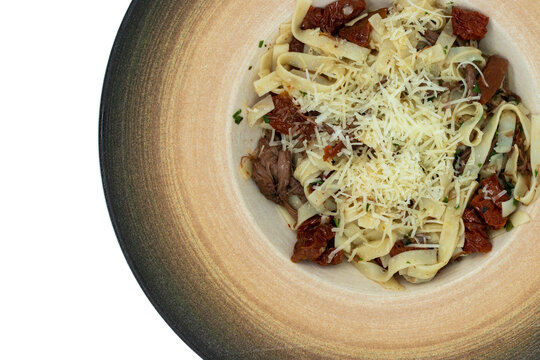 Gourmet pasta tagliatelle with pulled beef, sun-dried tomatoes, and parmesan cheese in a designer ceramic bowl