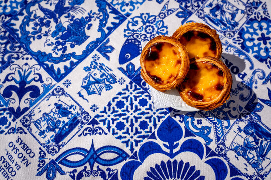 Pack of pastel de nata custard tarts overhead on blue pattern