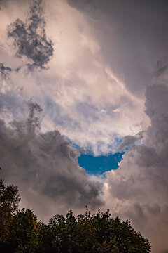 Dark clouds part to reveal a vibrant patch of blue sky above a serene landscape