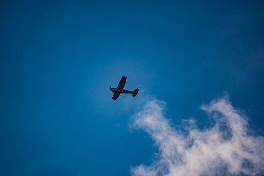 Flying high above, a small plane navigates the bright blue sky, surrounded by fluffy white clouds