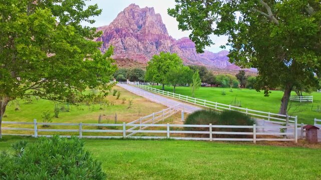 Gravel road bordered by white fences and green pastures toward rugged sandstone cliffs at Spring Mountain Ranch State Park Nevada