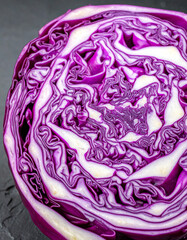 Obraz premium Macro cross section of a purple cabbage showing brain like geometric patterns on a dark stone surface.