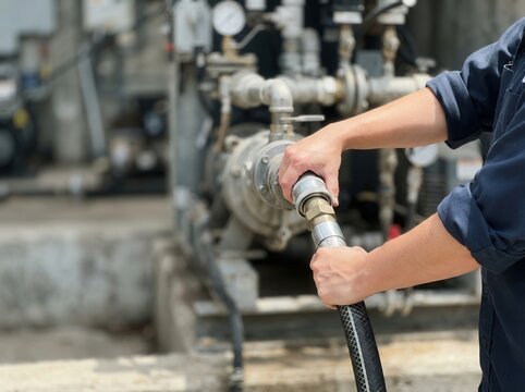 Technician Carefully Connecting a Heavy-Duty Industrial Hose to a Complex Mechanical Pump System for Efficient Liquid Transfer and Facility Maintenance