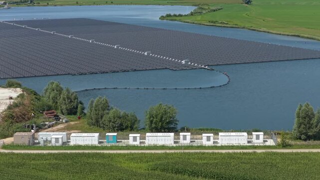 Aerial view of a large floating solar panel farm on a lake with its corresponding battery energy storage system on the shoreline