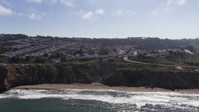Sweeping aerial footage captures dramatic cliffs, shimmering ocean waves, and Mussel Rock Park Beach under bright natural sunlight near Daly City, California for scenic stock use. Orbiting drone shot