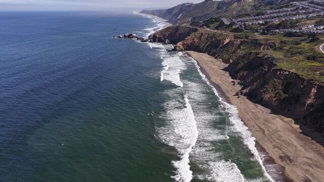 High-angle view showing the beautiful Pacific Ocean coastline with waves breaking on the sandy beach near the cliffs of Mussel Rock Park in Daly City, California on a sunny day