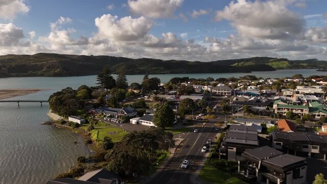 Stunning 4K 60fps drone footage capturing cars driving through the streets of Raglan at sunset. This aerial view showcases the peaceful coastal town traffic bathed in warm golden hour light