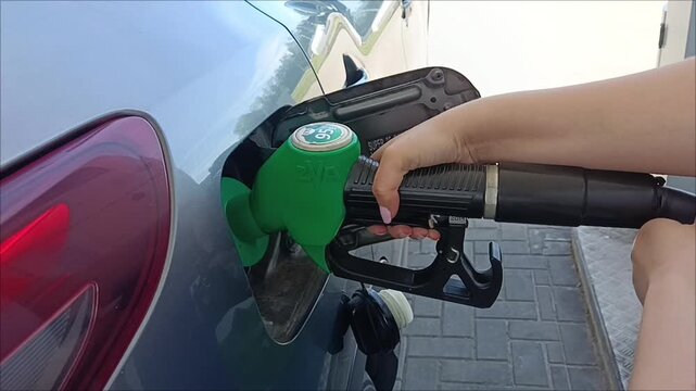 Filling the car. Close-up of a person refilling a passenger car at a gas station with a green fuel nozzle. Refueling service, rising energy cost concept.