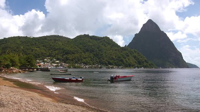 Cinematic beachside view of Soufri&egrave;re Bay in Saint Lucia, with pebbled shores, small fishing boats floating on calm water, and the iconic Petit Piton rising in the background.