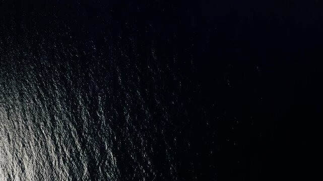 Top down drone shot of deep open Pacific Ocean water off Teahupoo, Tahiti, dark rippling texture with faint light reflecting across the surface.
