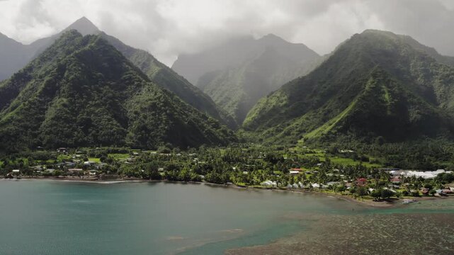 Aerial drone glides over misty peaks and taro plantations near Teahupoo, Tahiti, terraced green fields following the valley floor toward the coast.