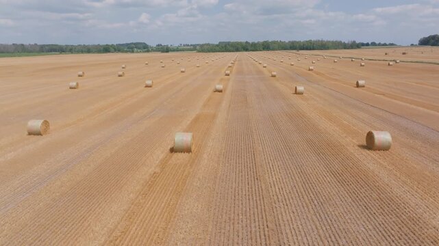The camera flies smoothly over a harvested agricultural field, passing close to a large round straw bale. Parallel tracks pattern the golden ground in Bruce County, Ontario.