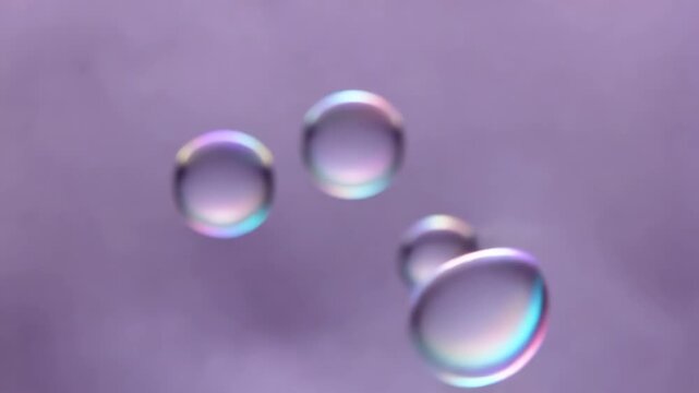 Colorful soap bubbles floating against a soft purple background, showcasing their iridescent surfaces and varying sizes in a continuous visual flow