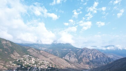 Cloud-filled blue sky above a distant mountain range, with billowy white clouds drifting across open space and misty ridgelines along the far horizon. © Daan De Vries