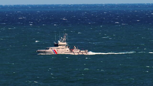 Coast guard patrol vessel navigating through choppy deep blue ocean waters.