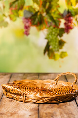 Naklejka premium Low wicker tray on rustic wooden table with blurred grapevine background for autumn harvest product mockup