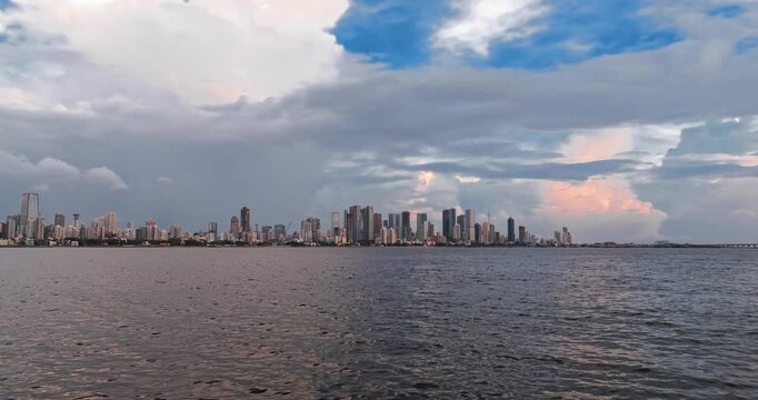 Beautiful sunset view of Mumbai, Maharashtra, with a dramatic orange sky illuminating the city skyline and calm waterfront. The glowing clouds, shimmering water, and striking evening cityscape.