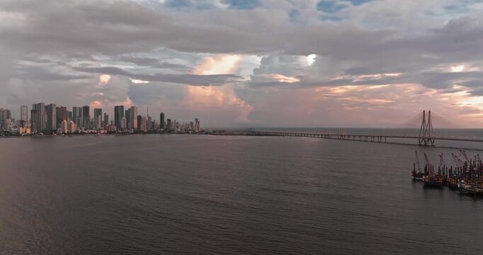 Beautiful sunset view of Mumbai, Maharashtra, with a dramatic orange sky illuminating the city skyline and calm waterfront. The glowing clouds, shimmering water, and striking evening cityscape.