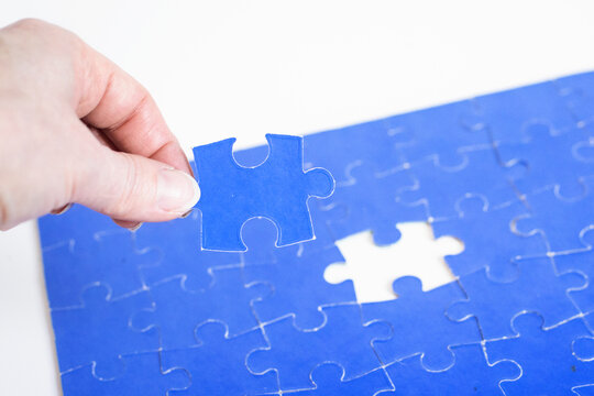 Hand placing last  puzzle piece in blue jigsaw, completion concept, close up