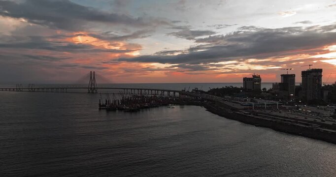 Beautiful sunset view of Mumbai, Maharashtra, with a dramatic orange sky illuminating the city skyline and calm waterfront. The glowing clouds, shimmering water, and striking evening cityscape.