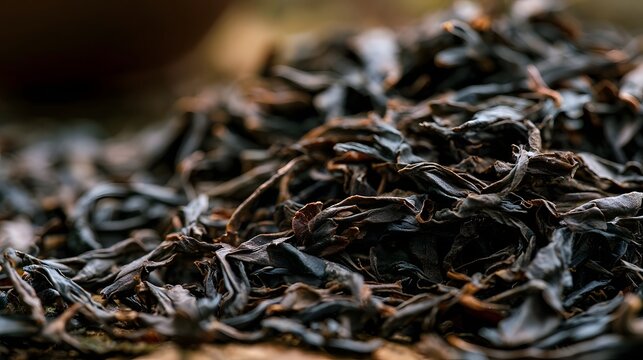 Close up of dark  curled dry tea leaves with warm lighting highlighting their textured surface and layered arrangement