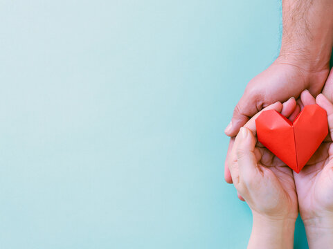 Hands gently offering a red paper heart against a soft blue background Generative AI
