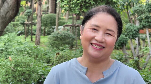 Happy and relaxed middle aged asian woman smiling in green park scene