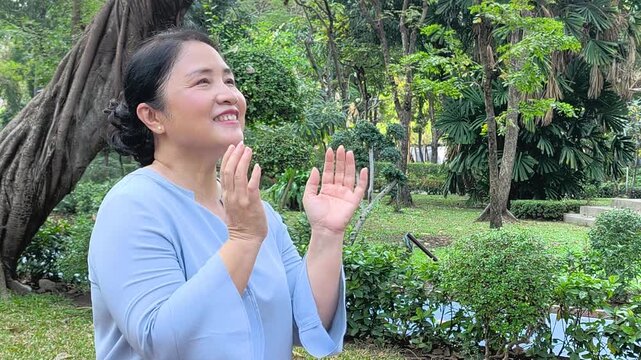 Happy and healthy middle aged asian woman breathing fresh clean air in green park during summer, concept of wellness, clean air and sunlight exposure for health