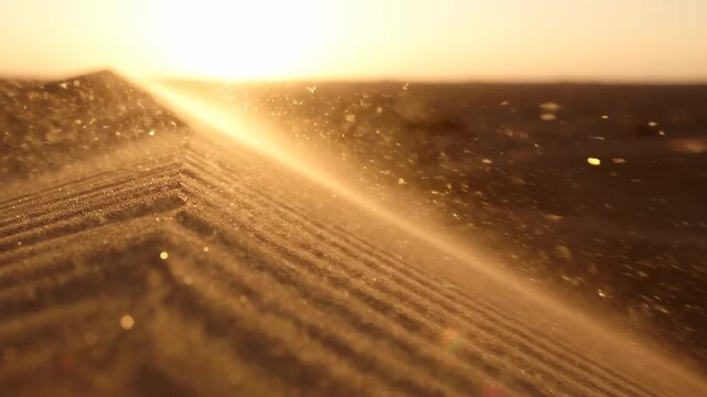 Wind blowing golden sand particles over desert dune at sunset