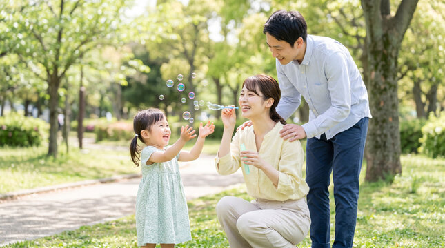 新緑の公園でしゃぼん玉を吹いて遊ぶ笑顔の家族