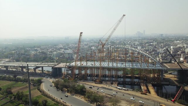 Aerial drone view of an under-construction arch bridge in Delhi, showcasing large-scale infrastructure development. Modern construction techniques, rapid urbanisation and connectivity in India city.