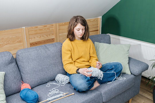 Teen girl knitting wool yarn on couch at home