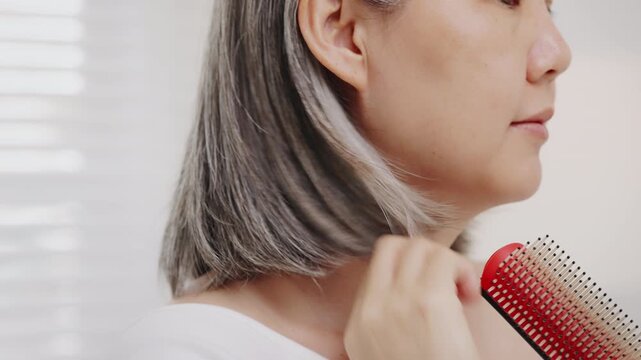 Close-up shot Asian mature woman with natural grey hair gently brushes her short hair.