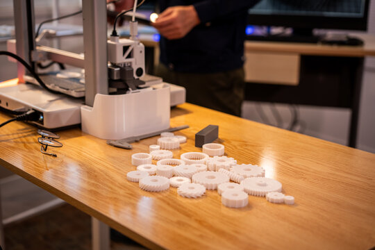 3d printer in a workshop with white plastic gears on a wooden table, showing product development, prototyping, and small-scale manufacturing.