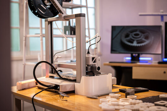 Desktop 3d printer or prototyping machine in a modern workshop with monitor, cables and small printed parts on a wooden table