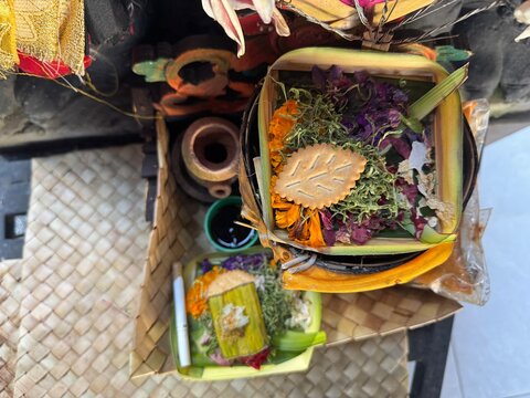 Traditional Balinese offering with colorful flowers, leaves and small containers in a woven basket.