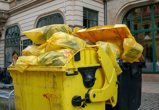 Yellow bins with yellow plastic waste bags ready for collection in an urban area.