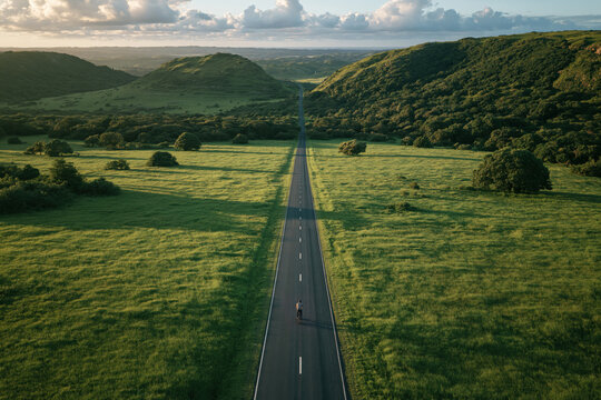 Rider travels down a long road surrounded by green hills under a blue sky in the afternoon