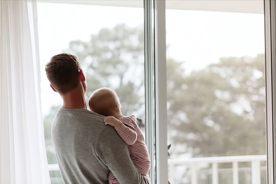 Father holding his baby looking out a window