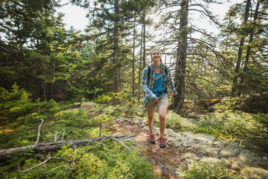 Happy young woman hiking on a sunny forest trail in Maine.