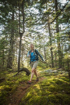 Smiling woman hikes on a mossy forest trail in the Maine woods.