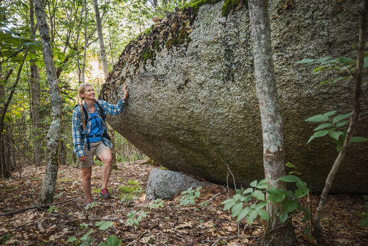 Smiling female hiker pauses by a large boulder, Maine.